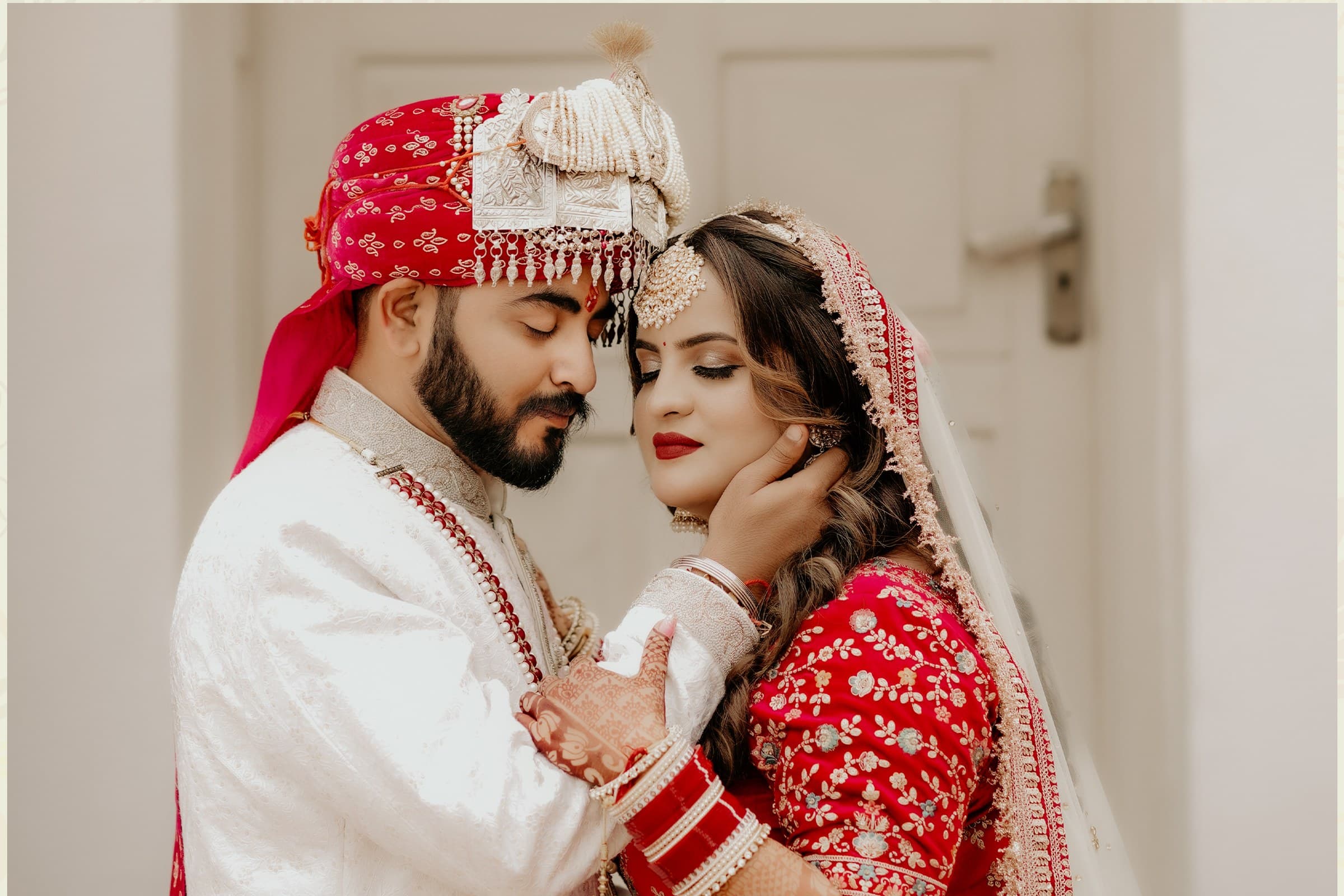 A bride and groom in traditional red wedding attire sharing a forehead-touching moment
