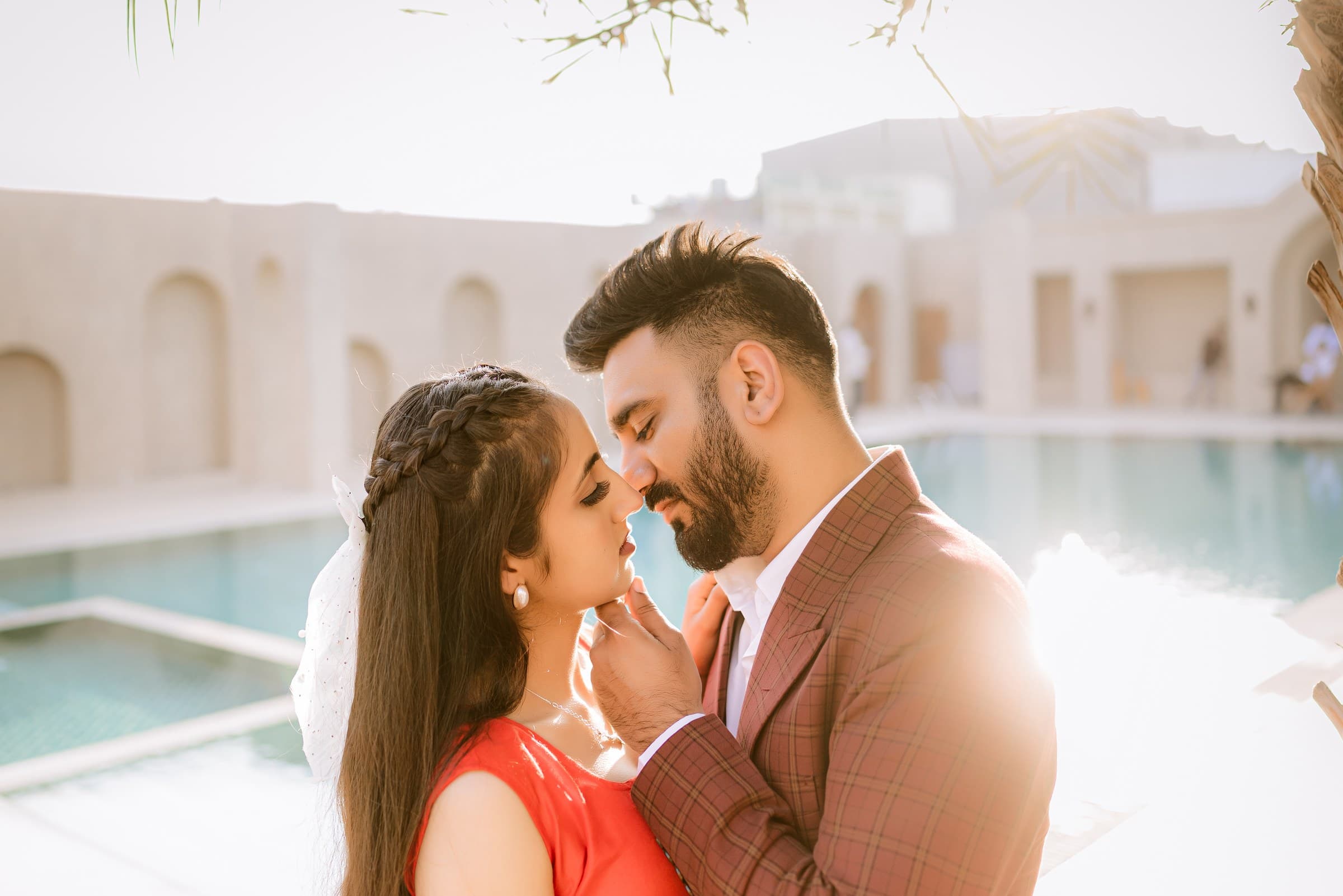 A couple sharing a nose-to-nose moment poolside, golden light behind them