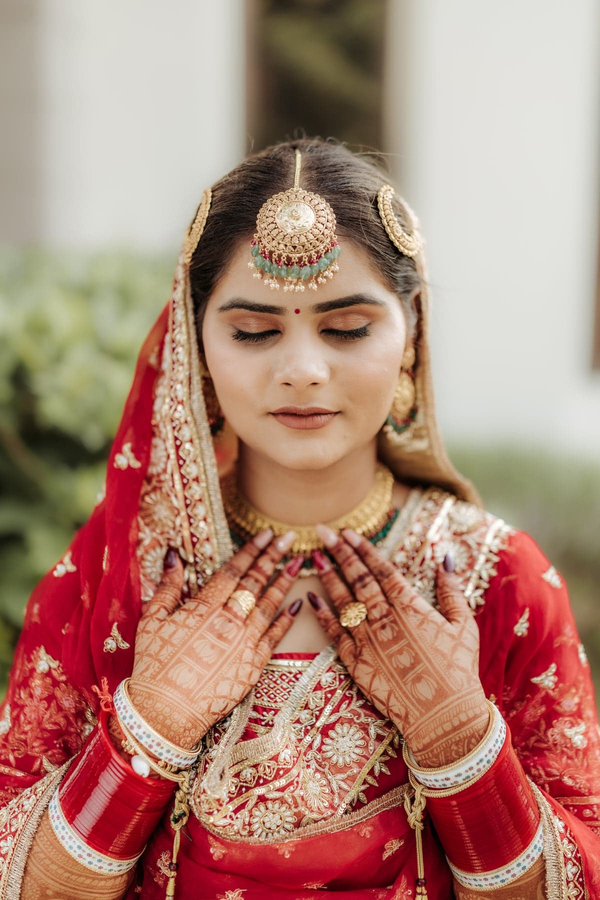A close bridal portrait in a red lehenga, hands folded
