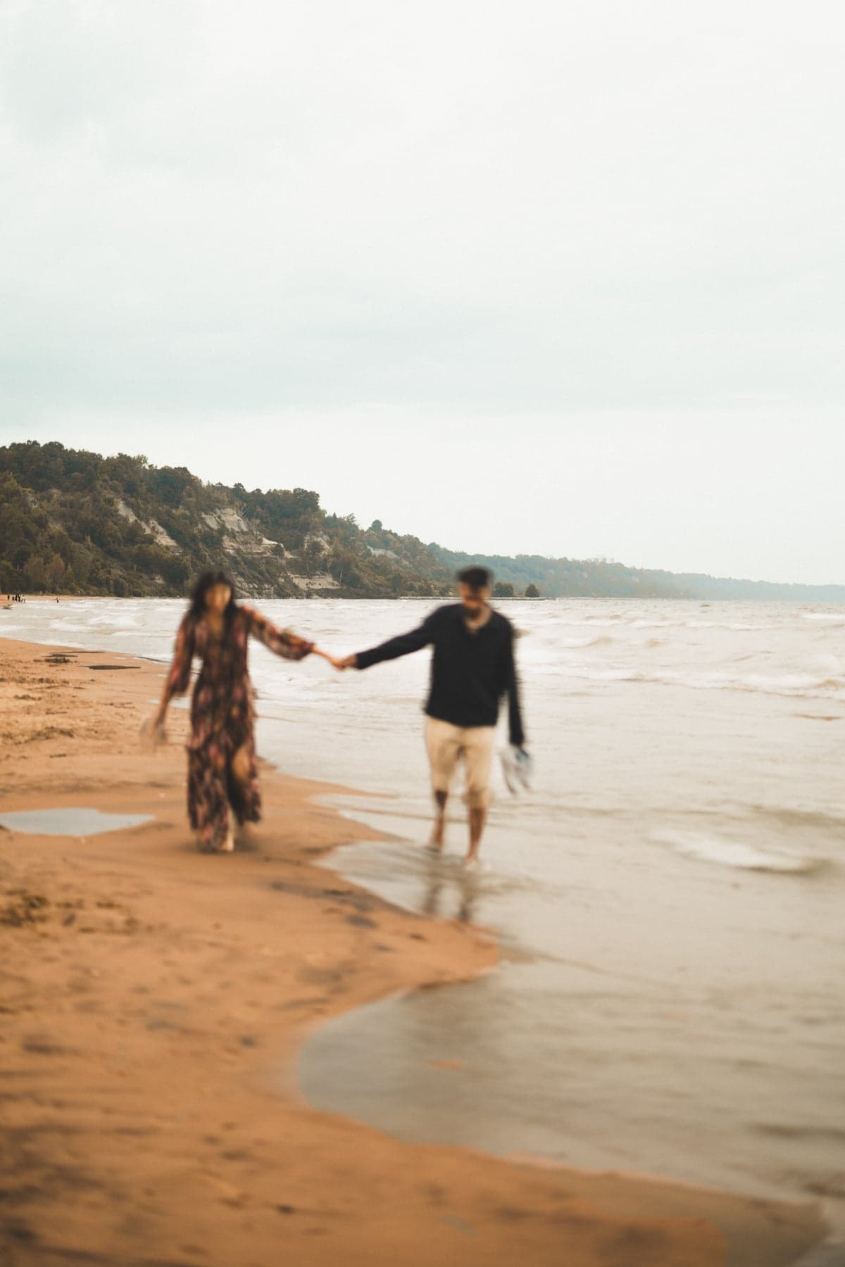 A couple walking hand in hand along a misty shoreline, soft focus