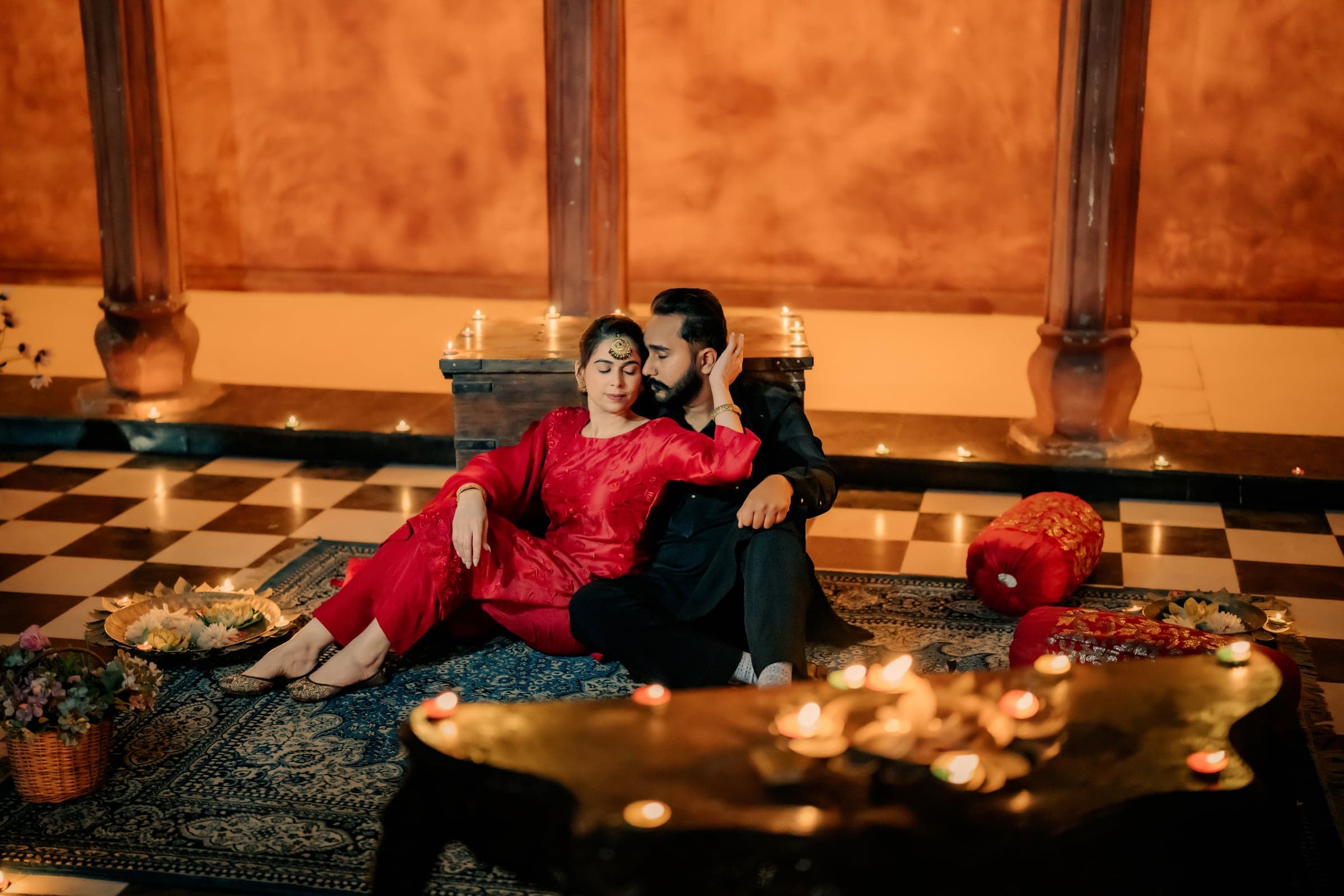 A couple seated close together on a candlelit rug inside a heritage courtyard