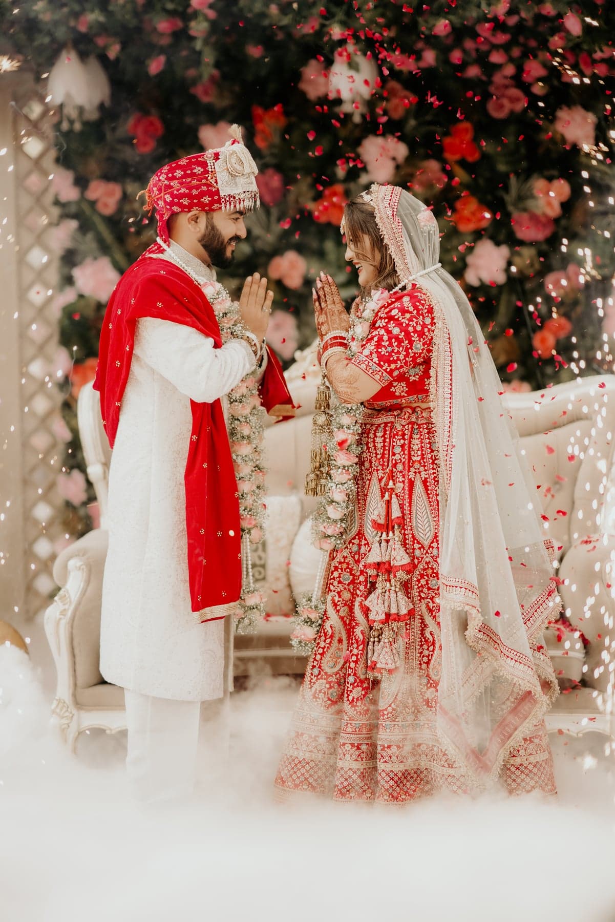 A bride and groom laughing together as rose petals fall around them