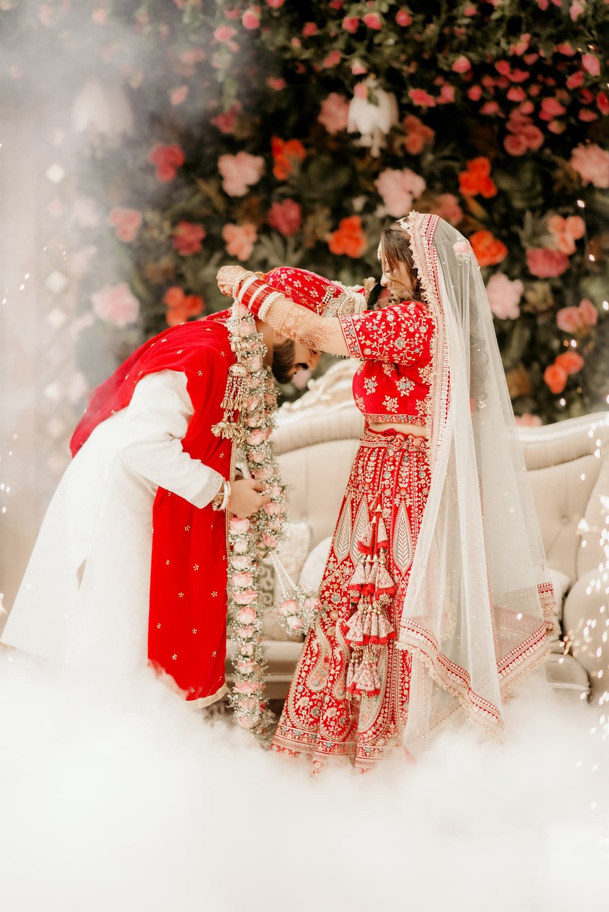A bride and groom exchanging garlands as rose petals fall