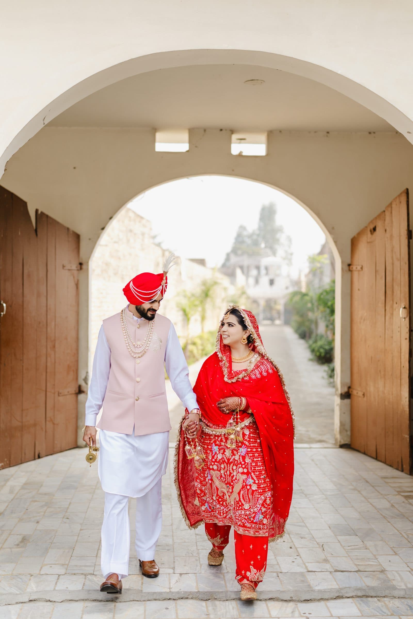 A bride and groom walking hand in hand through a courtyard archway
